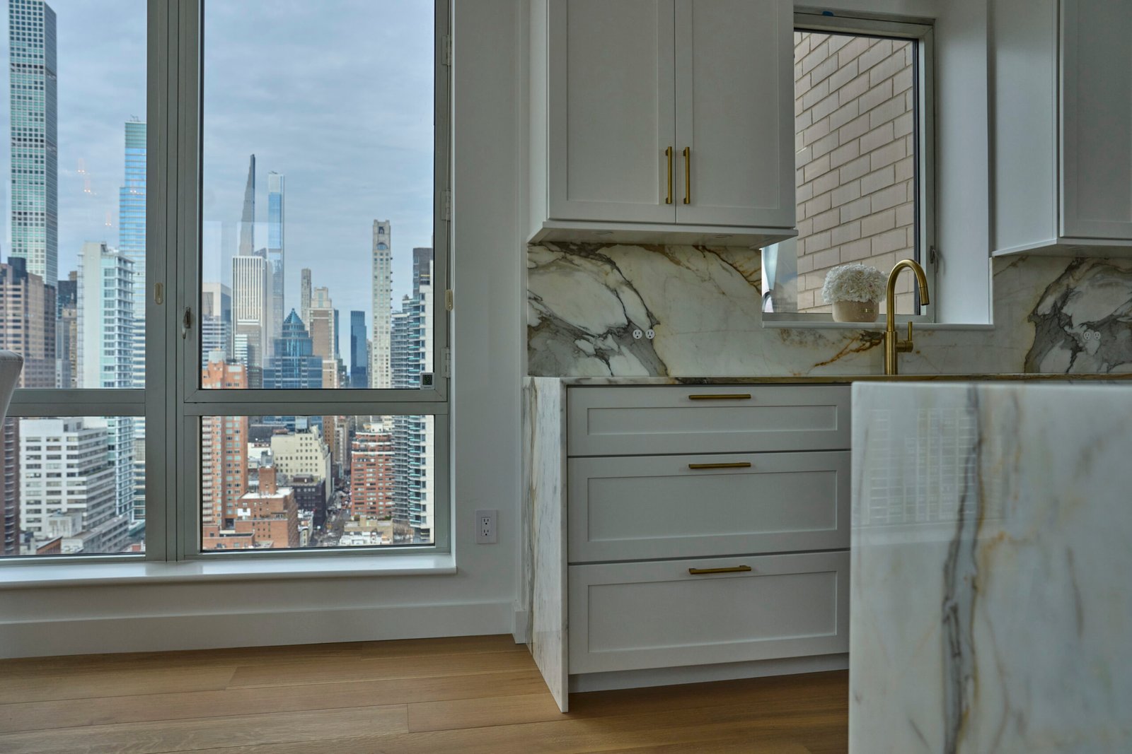 Custom natural stone kitchen island countertop and backsplash with white cabinetry, gold hardware, and New York City views
